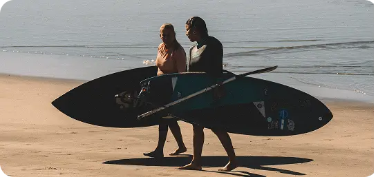 Dos surfistas de SUP cargando sus tablas en la playa en El Salvador